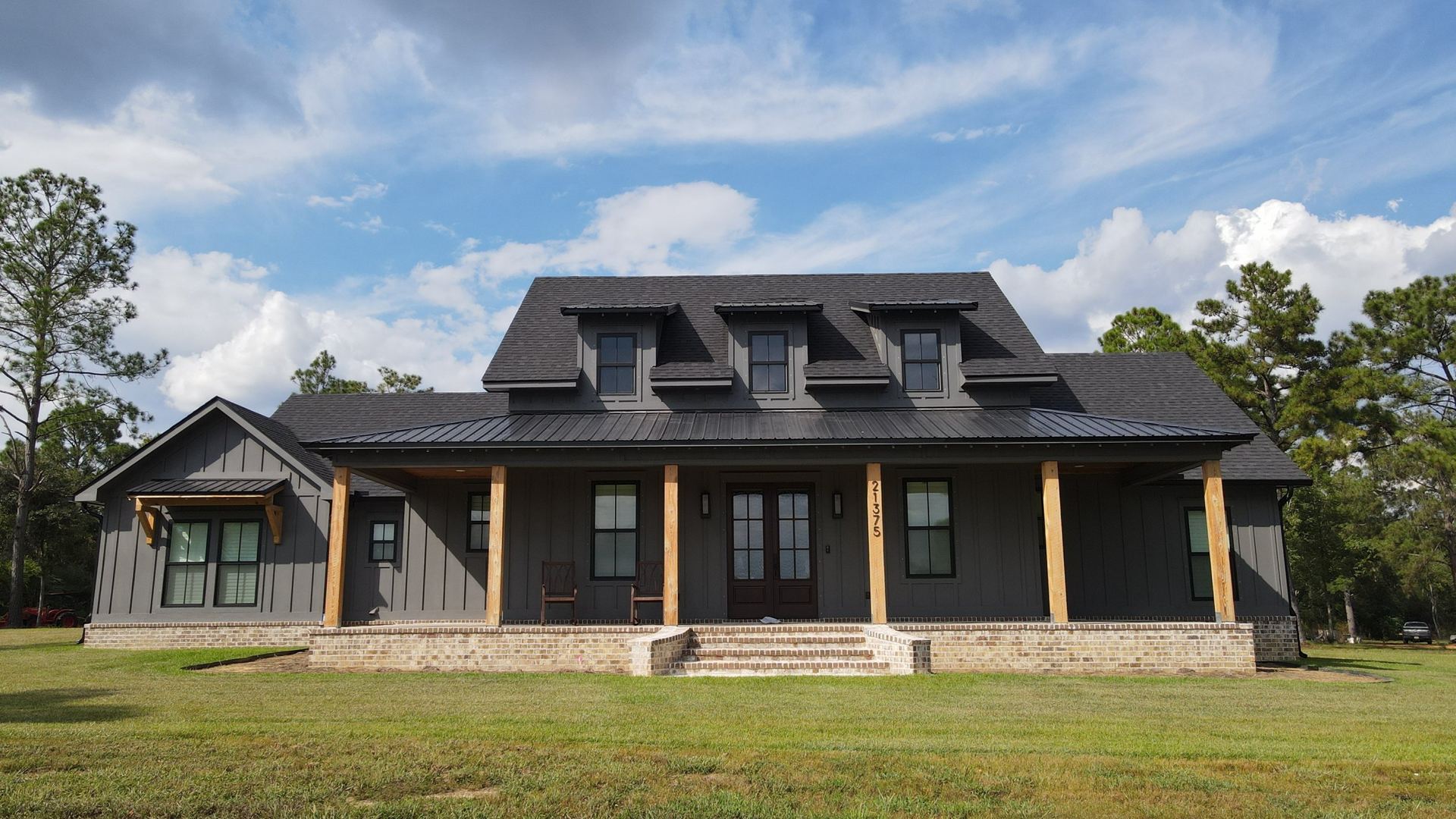 Aerial view of a farmhouse with a new shingle roof and black metal porch and dormer roofs
